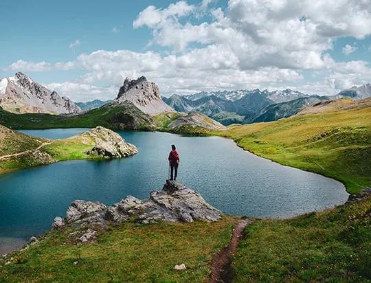 Une personne debout sur un rocher regardant au-dessus d’un lac avec des montagnes de lard en arrière-plan