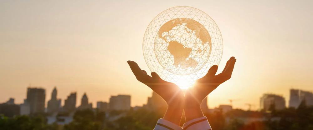 two hands holding up a globe in front of a sunset