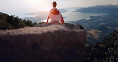 person sitting with a Canadian flag cape overlooking the landscape